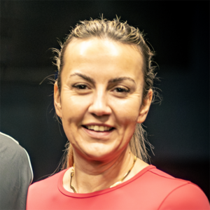 Eine Frau mit zurückgebundenen blonden Haaren lächelt in die Kamera.